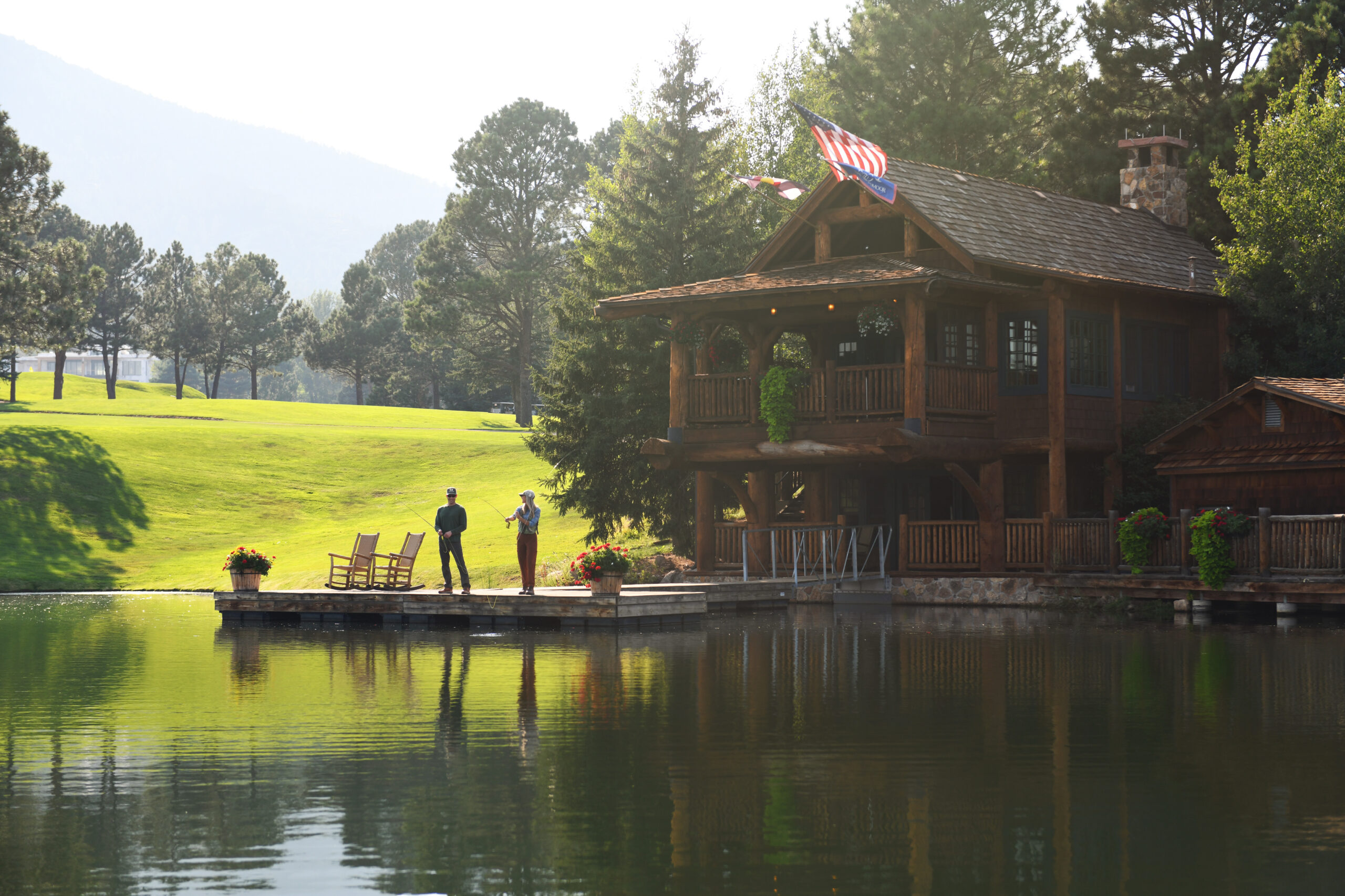 A wooden cabin with a fishing pier on a small lake next to a lawn