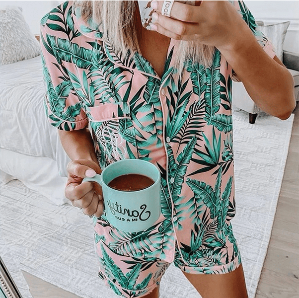 A cropped photo of a white woman wearing custom ShopILJ pajamas. They are pink with a tropical leaf pattern over top.