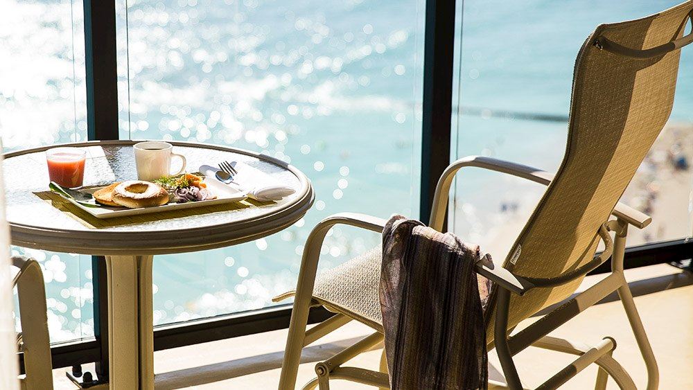 A deck chair and table on a patio at Outrigger Waikiki. The beach and ocean can be seen below. For marina meetings.