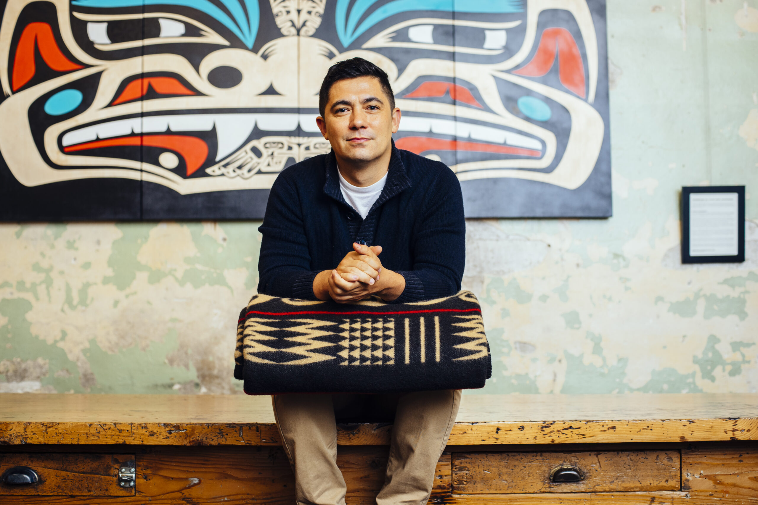 image of louie gong sitting down with black, gold-accented blanket