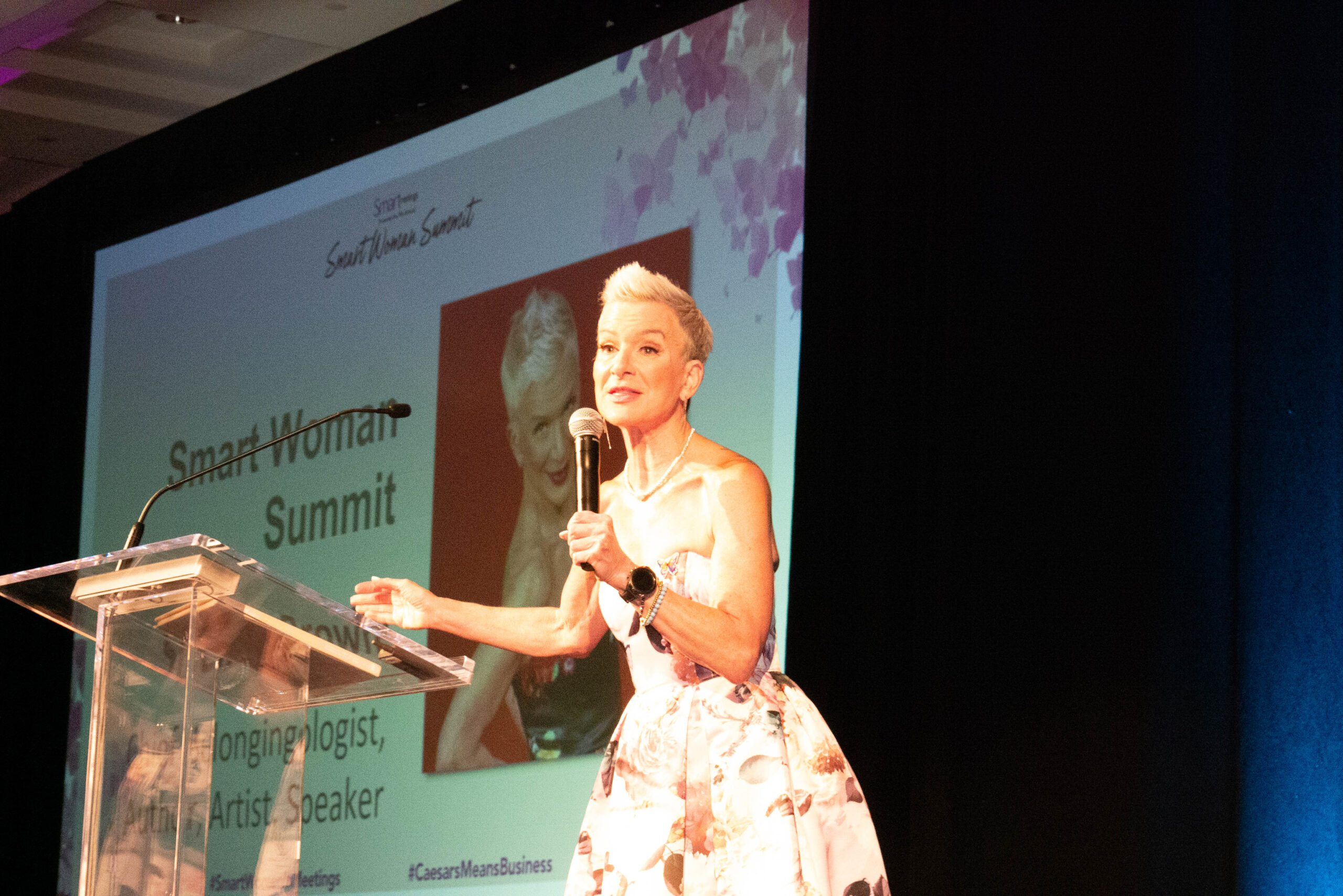 Judi Holler wearing floral dress, speaking on stage