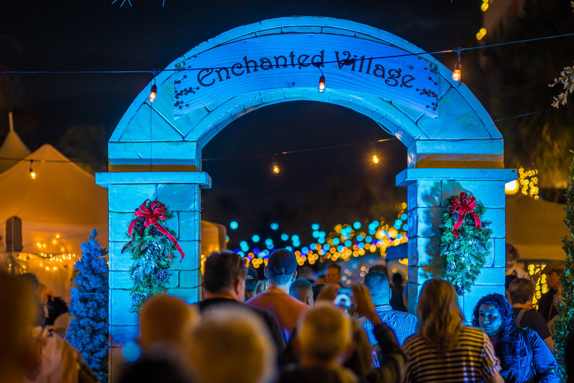 People walking through arch that reads "Enchanted Village" at Dickens on Centre