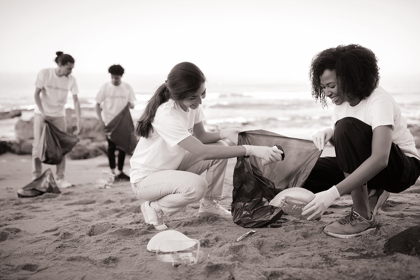 black and white image of four people on beach cleaning up for csr